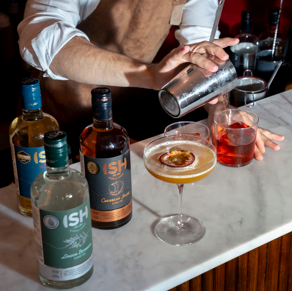 Bartender preparing an alcohol-free cocktail with ISH branded bottles on a marble counter.